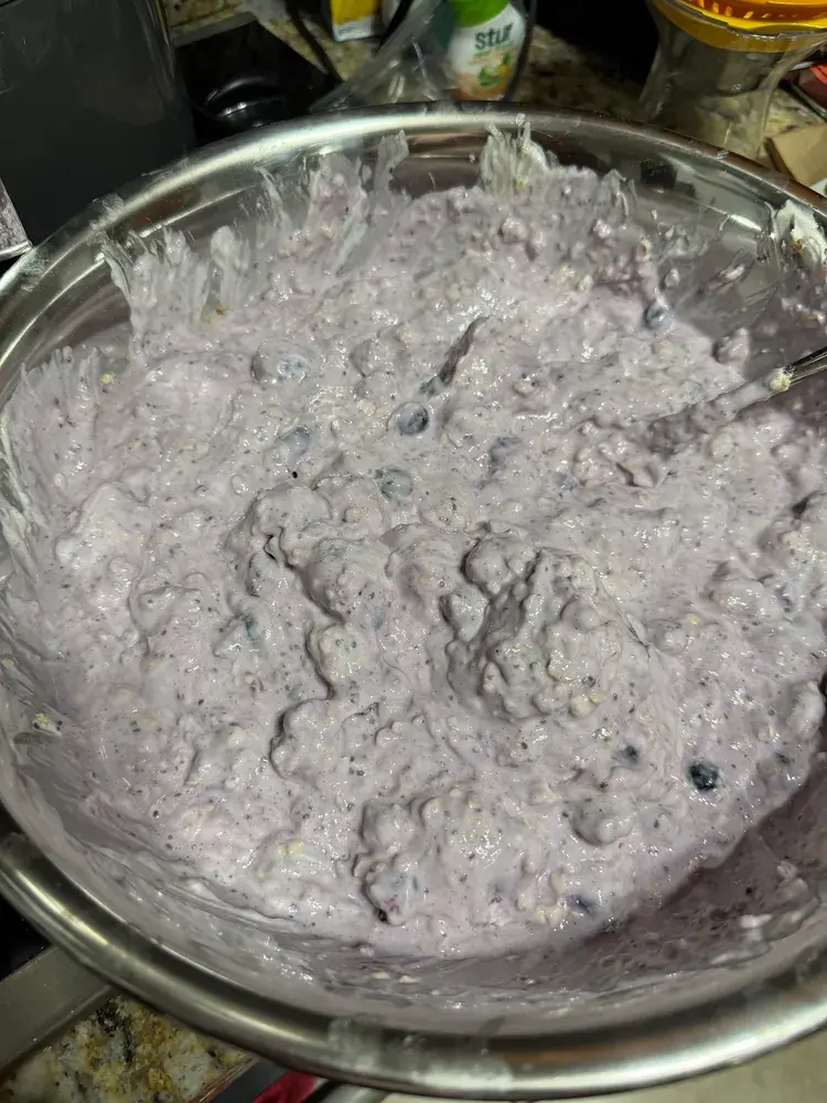 A large mixing bowl of yogurt, oats, and berries stirred together into a thick, gloopy batch